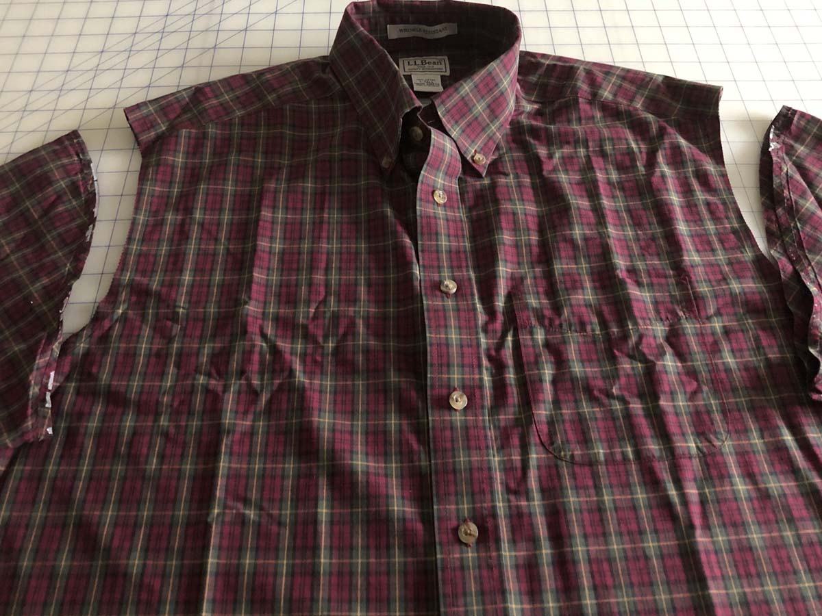 Shirt sleeves removed from red plaid shirt that is lying on gridded worksurface