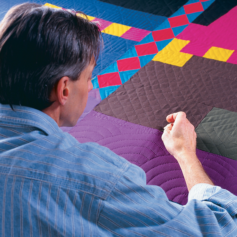 Man quilting freehand on a quilt on a frame